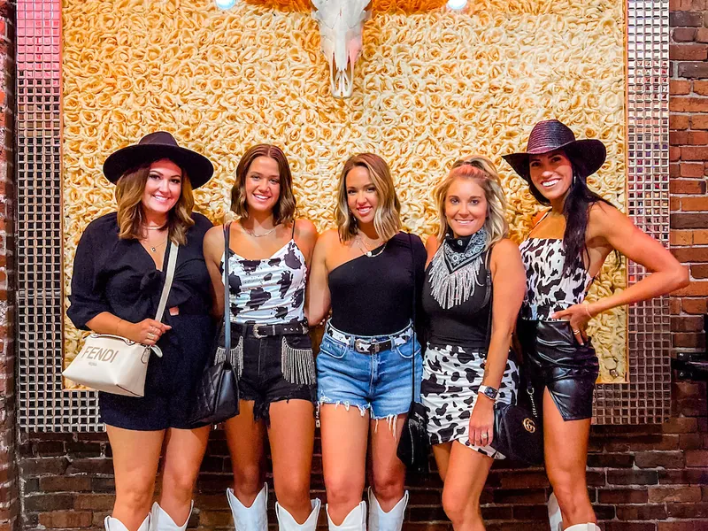 A group of friends in cowboy boots posing under a Nashville neon sign